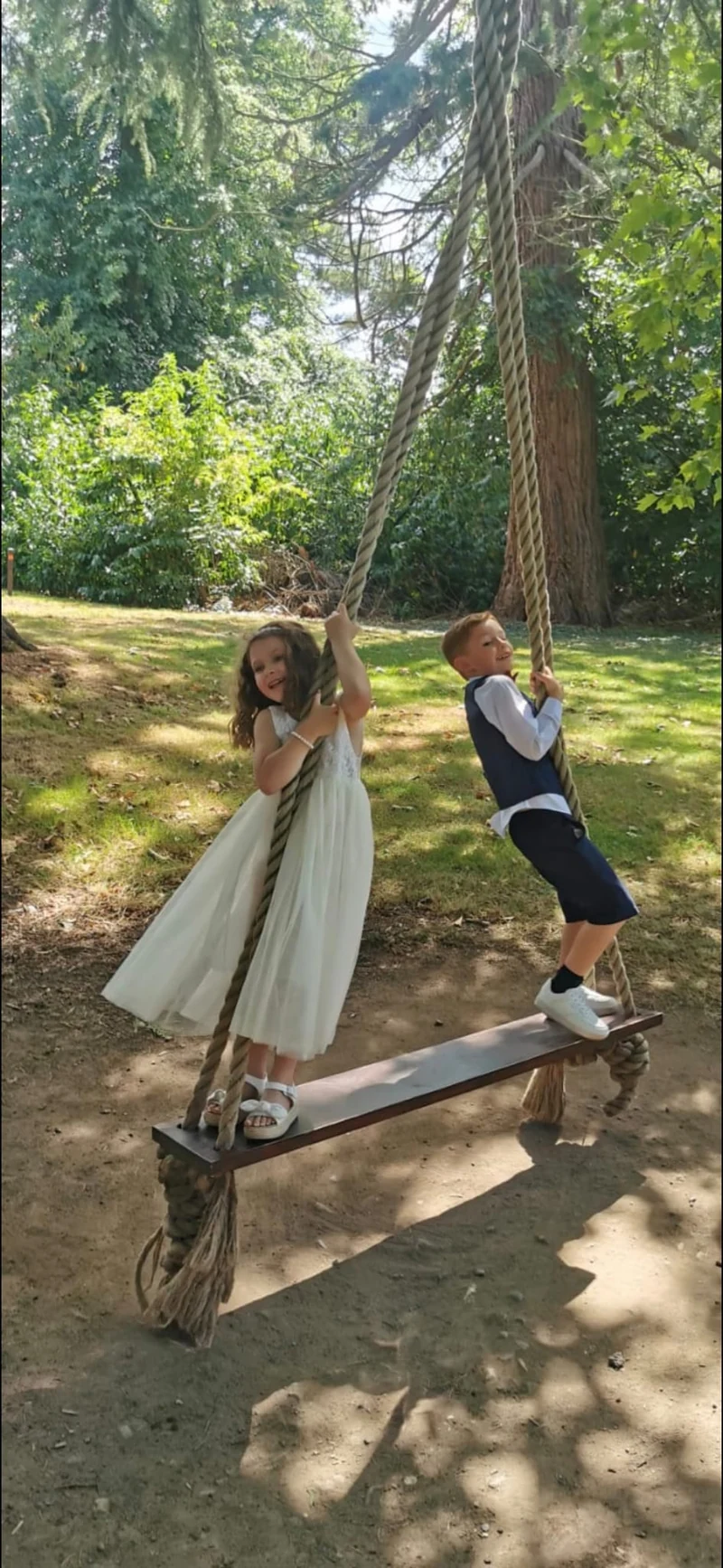 Two children enjoying a garden swing in their celebration clothes